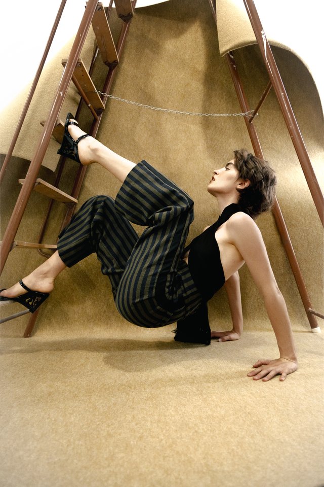 Model mit schwarzem Oberteil und gestreifter Hose neben einer Leiter